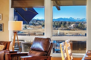 A room with a large window, a leather chair, a lamp, and a view of mountains.
