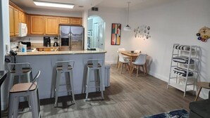 A modern kitchen with wooden cabinets, a stainless steel refrigerator, and a bar area with stools.