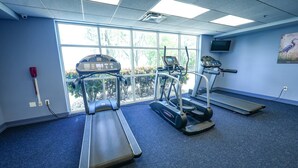 Ein Fitnessraum mit Laufbändern, einem Ergometer und einem Fernseher an der Wand.