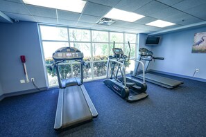 Ein Fitnessraum mit Laufbändern, einem Ergometer und einem Fernseher an der Wand.