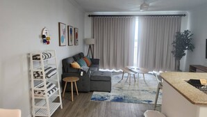Ein modernes Wohnzimmer mit einem grauen Sofa, einer weißen Regaleinheit, einem kleinen runden Tisch und einer Küchenzeile mit einer Granit Arbeitsplatte.
