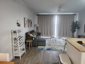 Ein modernes Wohnzimmer mit einem grauen Sofa, einer weißen Regaleinheit, einem kleinen runden Tisch und einer Küchenzeile mit einer Granit Arbeitsplatte.