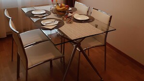 Un coin repas comprenant une table en verre, quatre chaises, un panier de fruits et un luminaire fixé au mur.