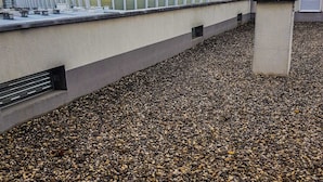 Une terrasse sur le toit avec un revêtement de gravier, un bâtiment moderne à la façade incurvée et un ciel dégagé.
