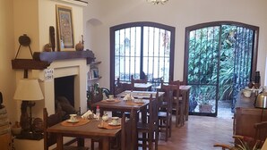 A spacious dining area with wooden flooring, a fireplace, and a large window with a view of greenery. - Posta del Ángel (Salta)