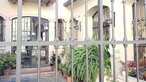 A courtyard with a wrought iron gate, potted plants, and a building with balconies and large windows. - Posta del Ángel (Salta)