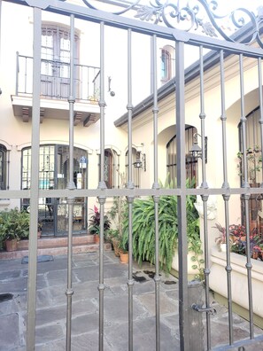 A courtyard with a wrought iron gate, potted plants, and a building with balconies and large windows. - Posta del Ángel (Salta)