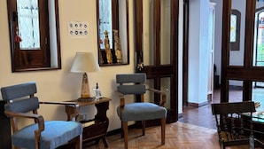 Een kamer met houten vloeren, twee blauwe fauteuils, een houten tafel met een lamp en grote spiegels aan de wanden.
