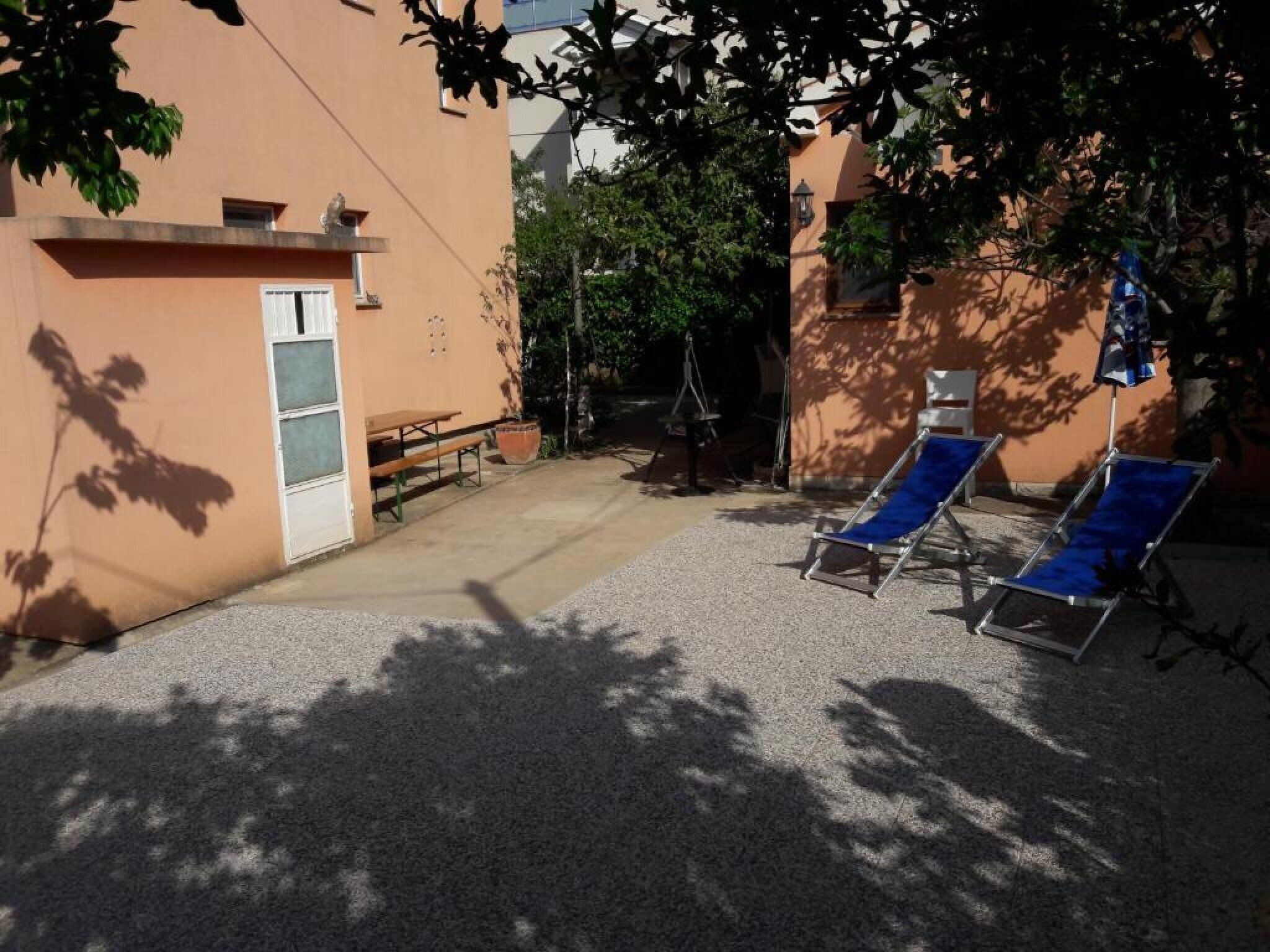 A courtyard with a bench, a table, and two sun loungers.