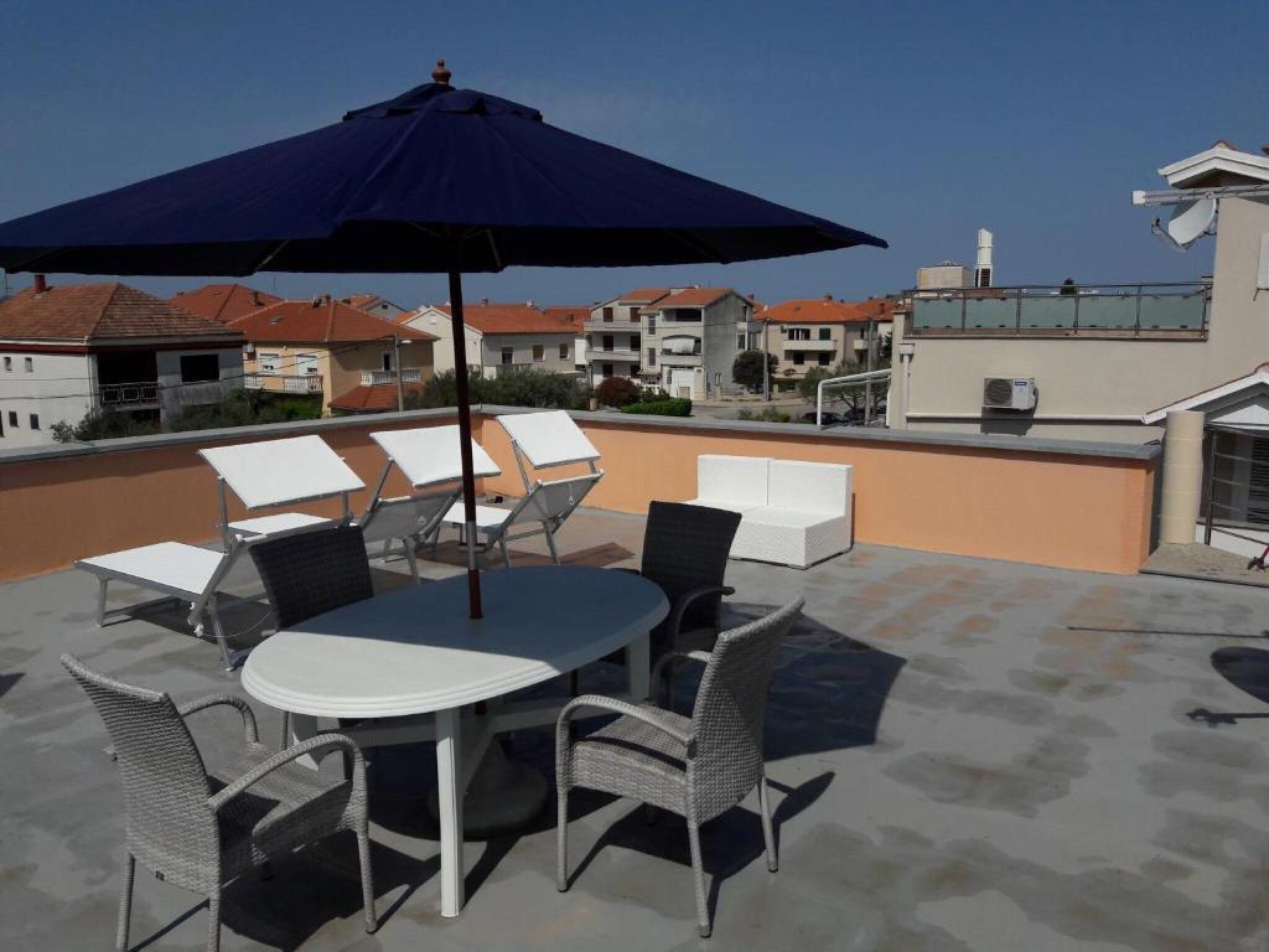 A rooftop terrace with a table and chairs, an umbrella, and a view of surrounding buildings.