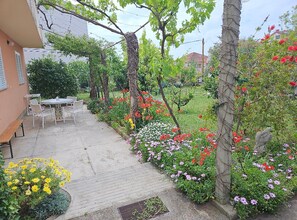 A garden with a patio table and chairs, surrounded by various flowering plants and trees. - Apartments Amalia (Zadar)