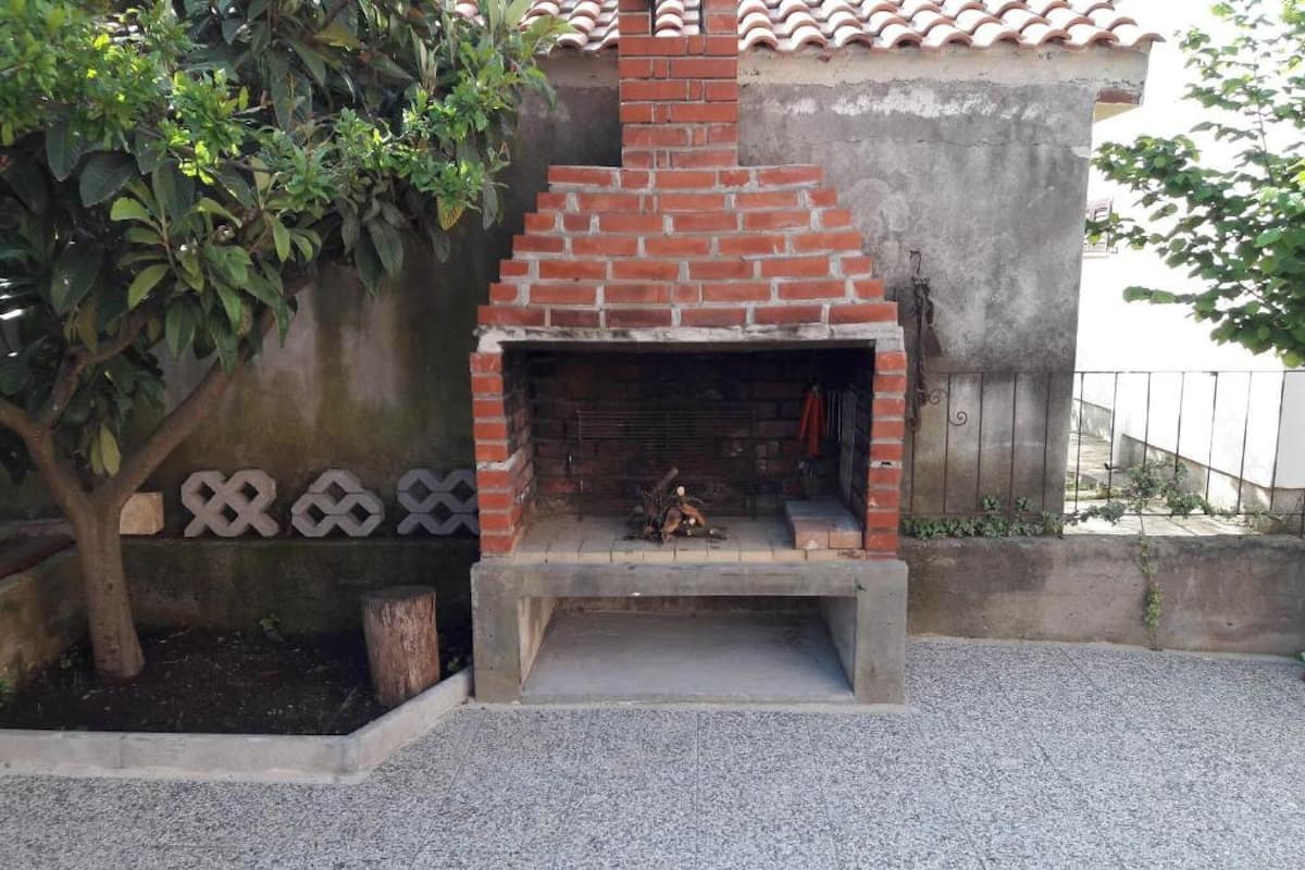 A brick-built outdoor fireplace with a stone bench in front, surrounded by a concrete wall and a tiled roof structure.