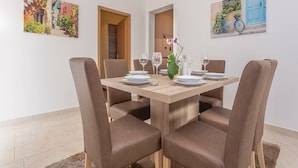 A dining area with a wooden table set for four, surrounded by brown upholstered chairs. There are paintings on the walls depicting colorful scenes. - Apartment Niko (Sibenik)