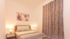 A bedroom with a bed, two bedside tables, a wall-mounted lamp, and a large window with curtains. - Apartment Niko (Sibenik)