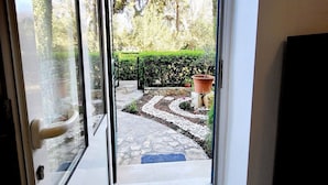 A modern entryway with a glass door leading to a garden area with a stone pathway, a blue mat, and a potted plant. - Green Terrace Apartment I (Dubrovnik)