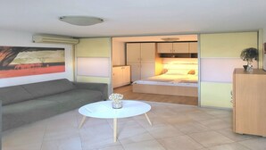 A compact living space with a sofa, a small round table, a bed, and a kitchenette. - Green Terrace Apartment I (Dubrovnik)