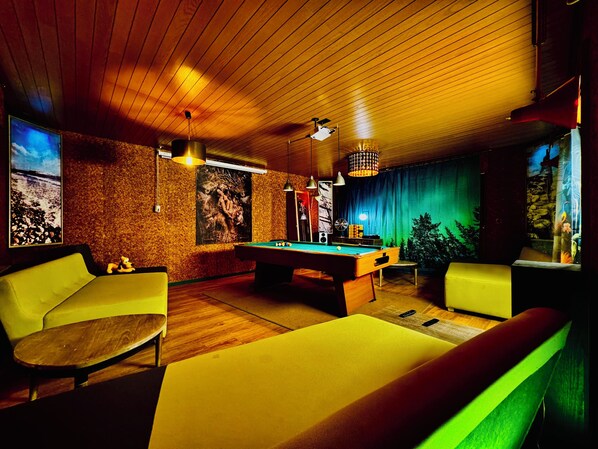 A pool table in a room with wooden walls and ceiling, two yellow armchairs, and a large painting on the wall. - Bookeinfach Villa Ferry (Bad Ems)