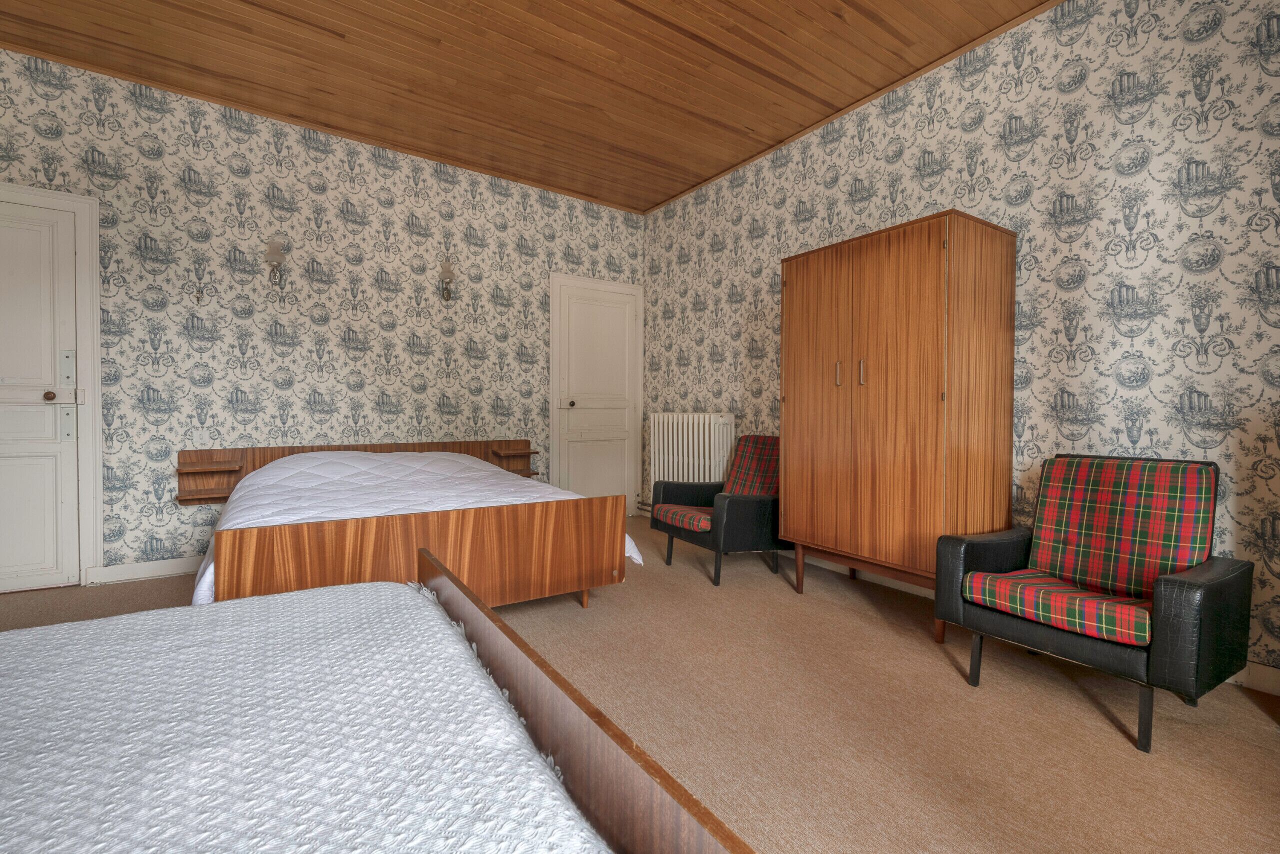 Ein Schlafzimmer mit zwei Betten, einem Kleiderschrank, einem Stuhl und einer Heizung.