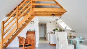 Una escalera de madera que sube a un nivel superior, un comedor con una mesa y sillas, y una cocina al fondo.