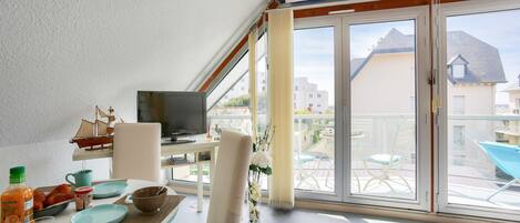 A modern room with a balcony, a dining table with breakfast items, a TV, and a view of the neighborhood.