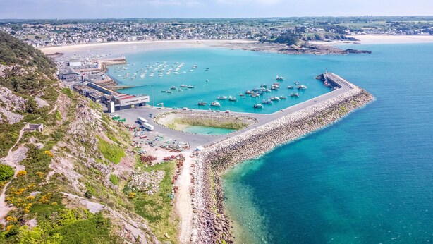 Vista aérea de un pueblo costero con puerto deportivo, costa rocosa y un faro.