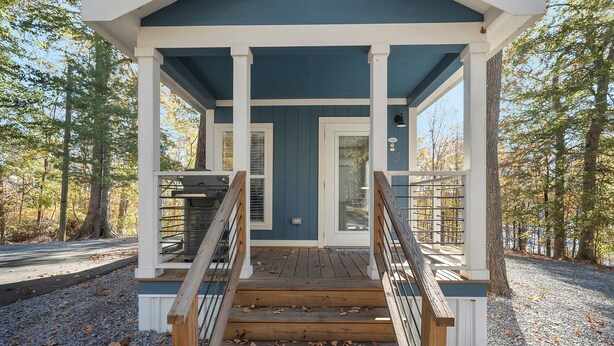 A covered wooden deck with a staircase leading to a door, surrounded by trees.