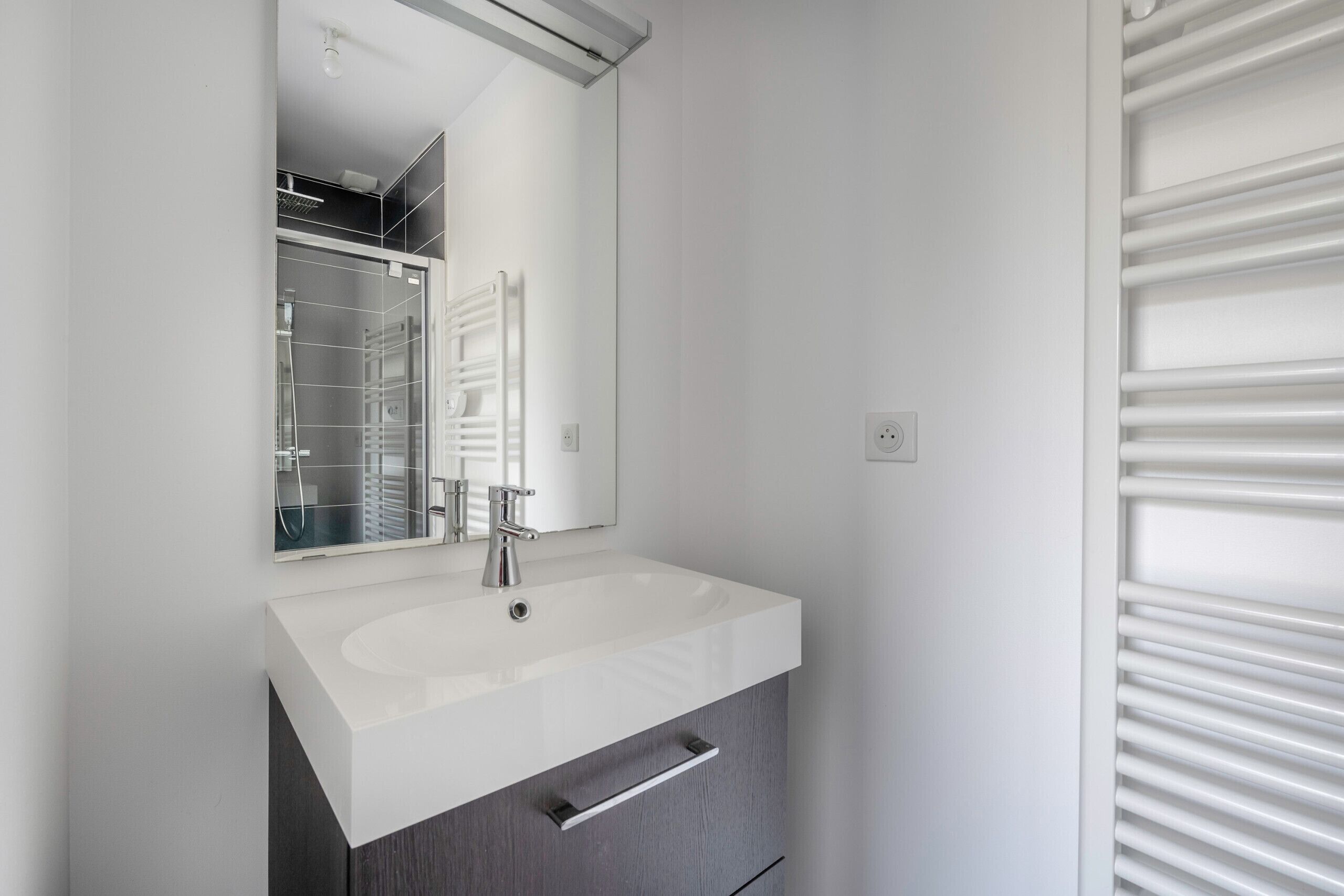 Une salle de bain moderne avec un lavabo blanc, un miroir et un porte-serviettes.
