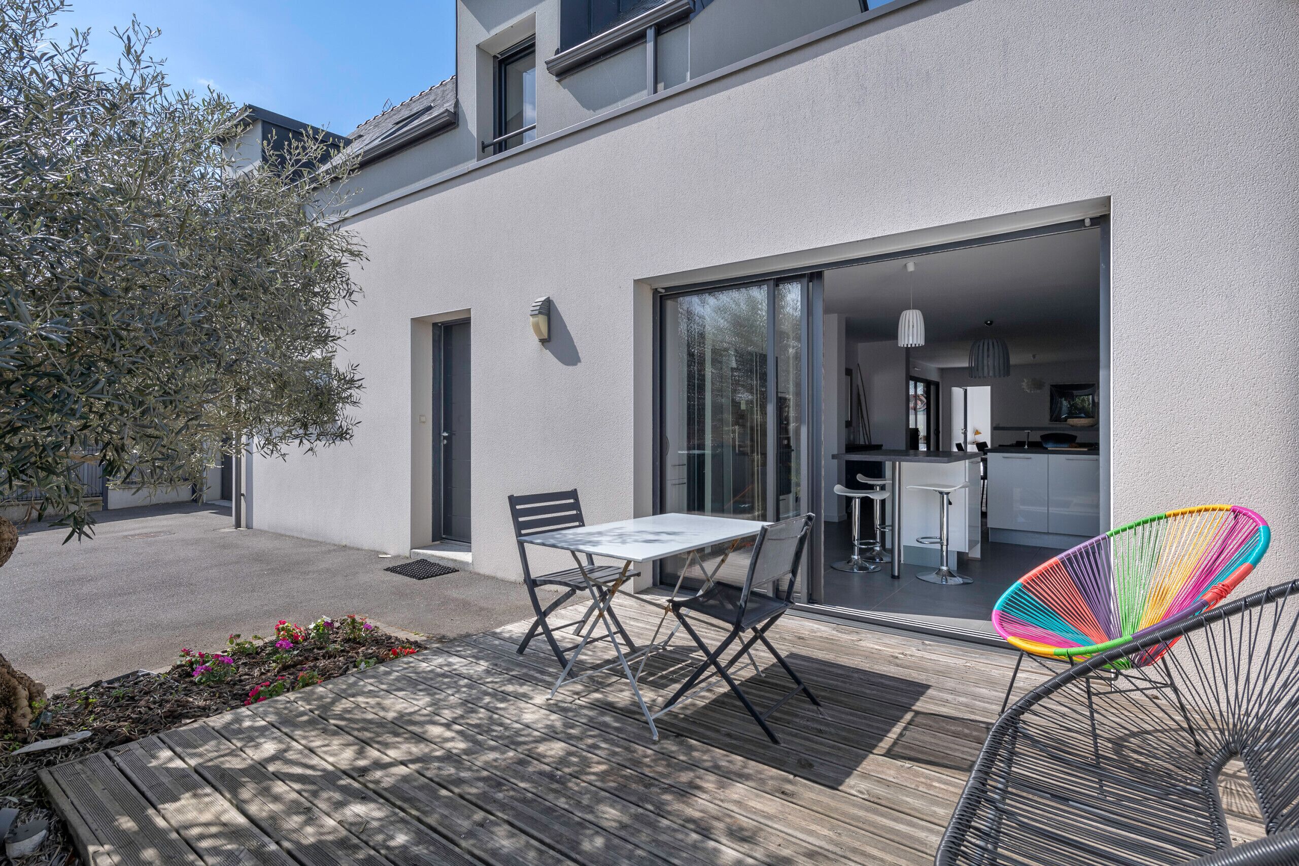 An outdoor patio with a table and chairs, a colorful chair, and a view into the house.