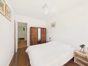 Une chambre à coucher comprenant un lit, une armoire en bois, une table de chevet, une lampe et une porte donnant sur une autre pièce.