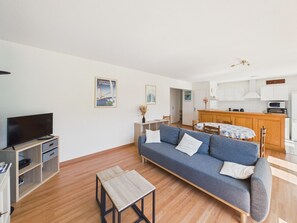 Un salon moderne avec un canapé, un téléviseur, un plancher en bois et une petite table.