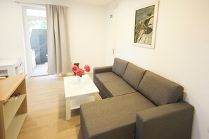 A living room with a grey sofa, a white coffee table, and a vase of pink flowers. - Apartment Goge (Dubrovnik)