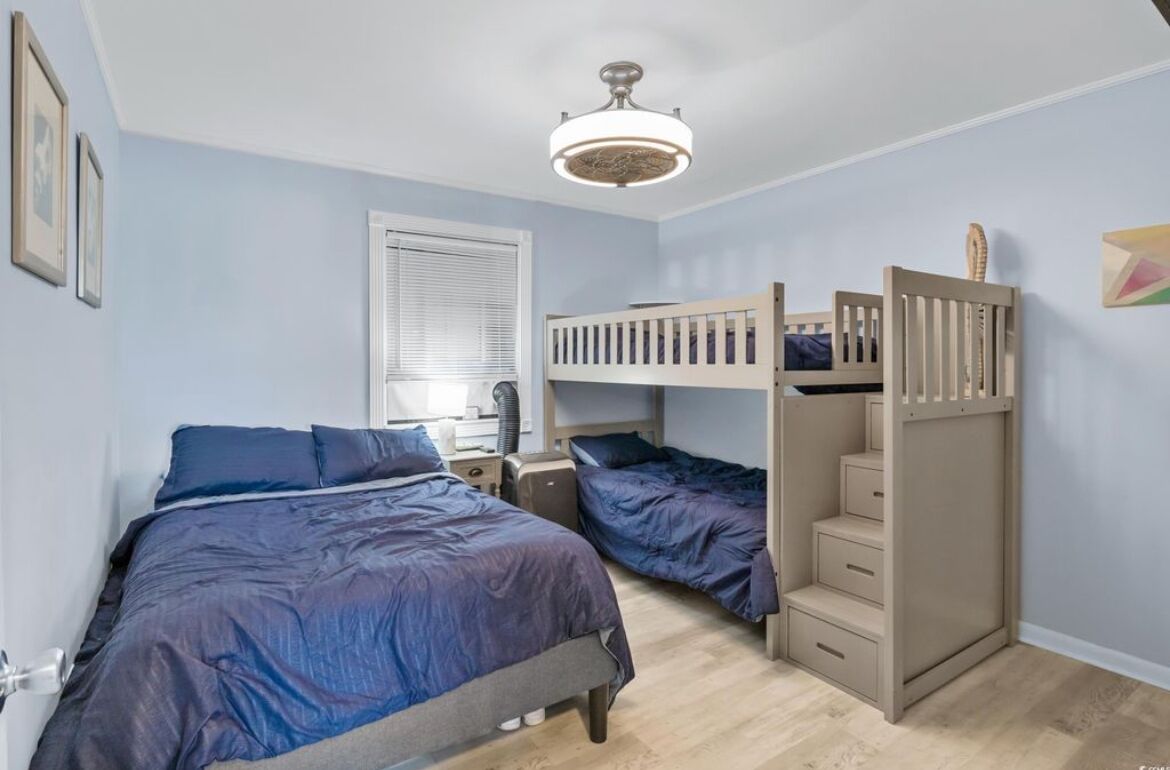 A bedroom with two bunk beds, a ceiling fan, a window with blinds, and a bed with a blue comforter.