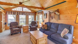 A log cabin interior with a wooden ceiling, a blue sofa, patterned armchairs, and a wooden coffee table. - Private Lakefront Emily Home w/ Yard & Fire Pit! (Emily)