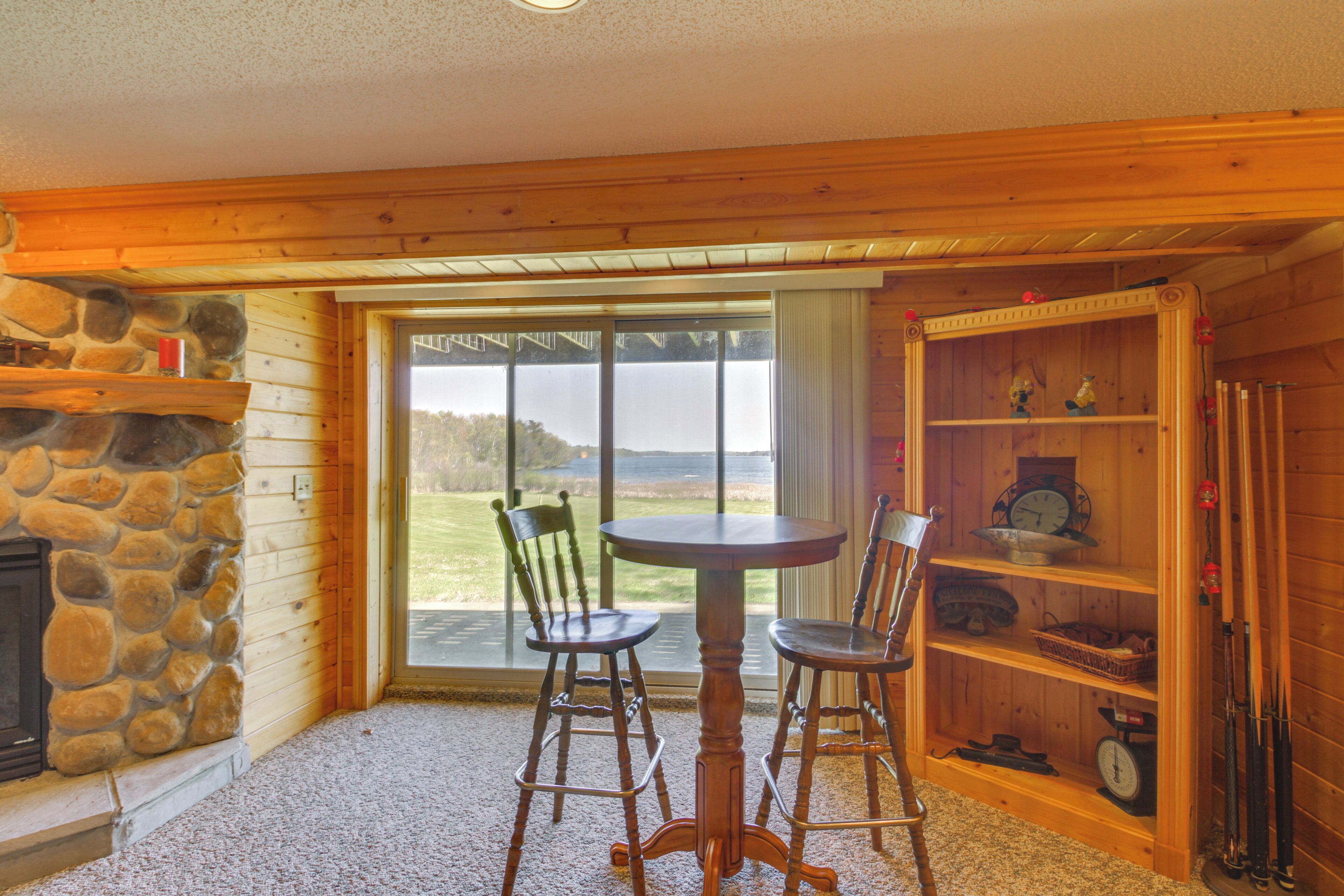 A cozy room with a stone fireplace, wooden walls, a round table with two chairs, and a bookshelf with fishing rods.
