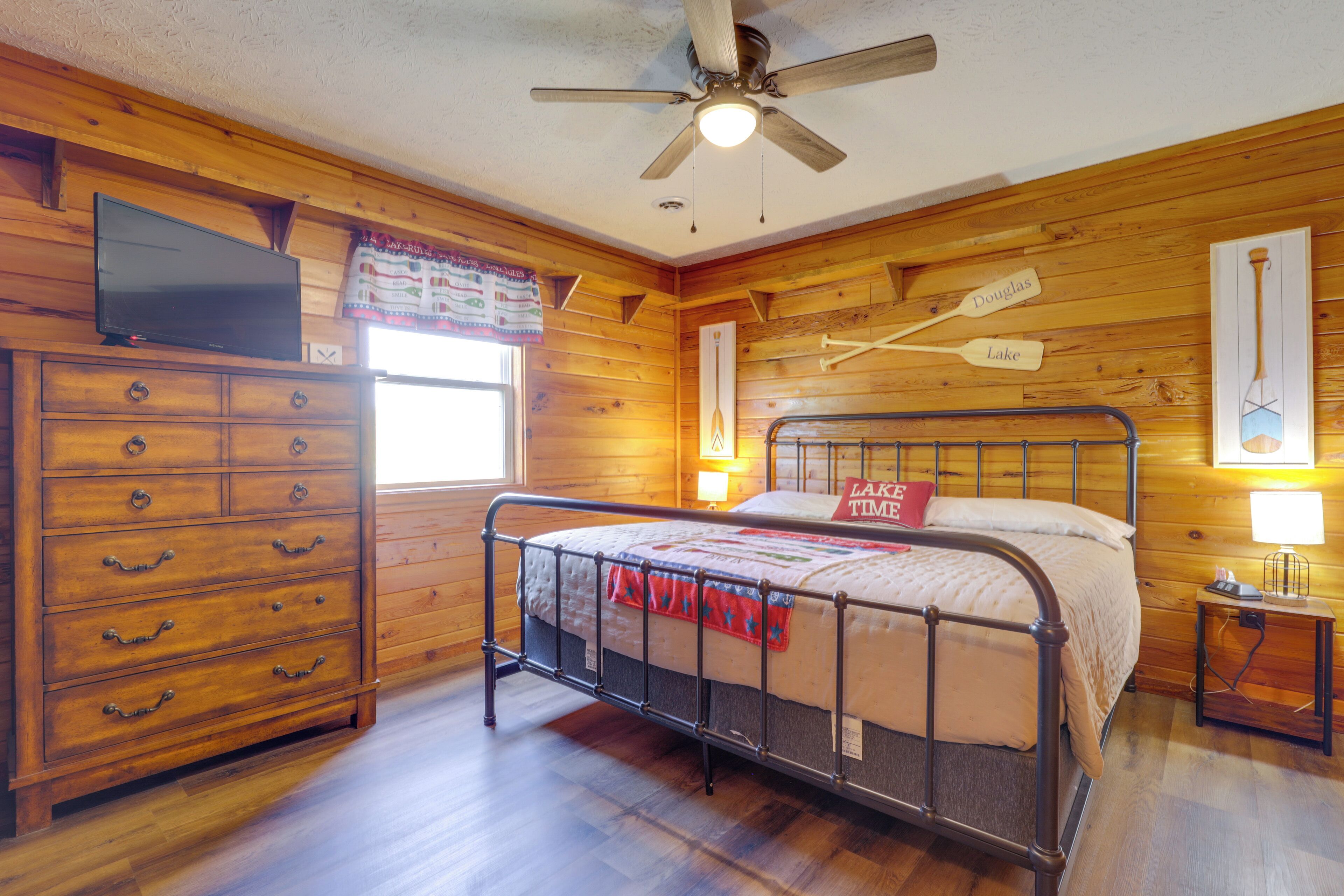 Een houten kamer in blokhutstijl met een metalen bed, een houten dressoir en een televisie aan de muur.