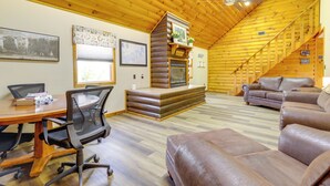 Ein Holzhütten-Interieur mit einem Holzespeisetisch, Bürostühlen, einem Kamin, einer Couch und einer Treppe.