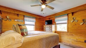 Ein Zimmer mit Holzwänden, einem Bett, einem Schmuckkästchen, einem Fernseher und dekorativen Ventilatoren.