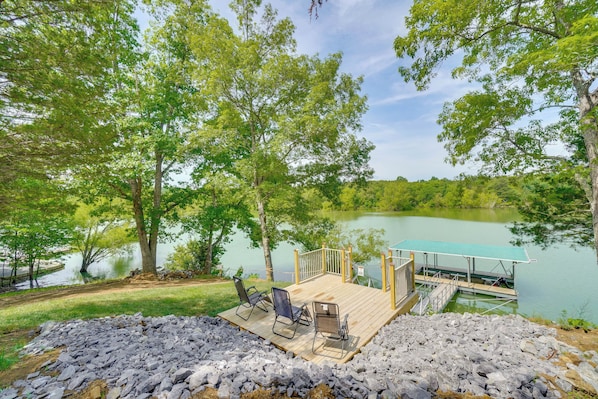 A wooden deck with chairs overlooking a lake, surrounded by trees.
