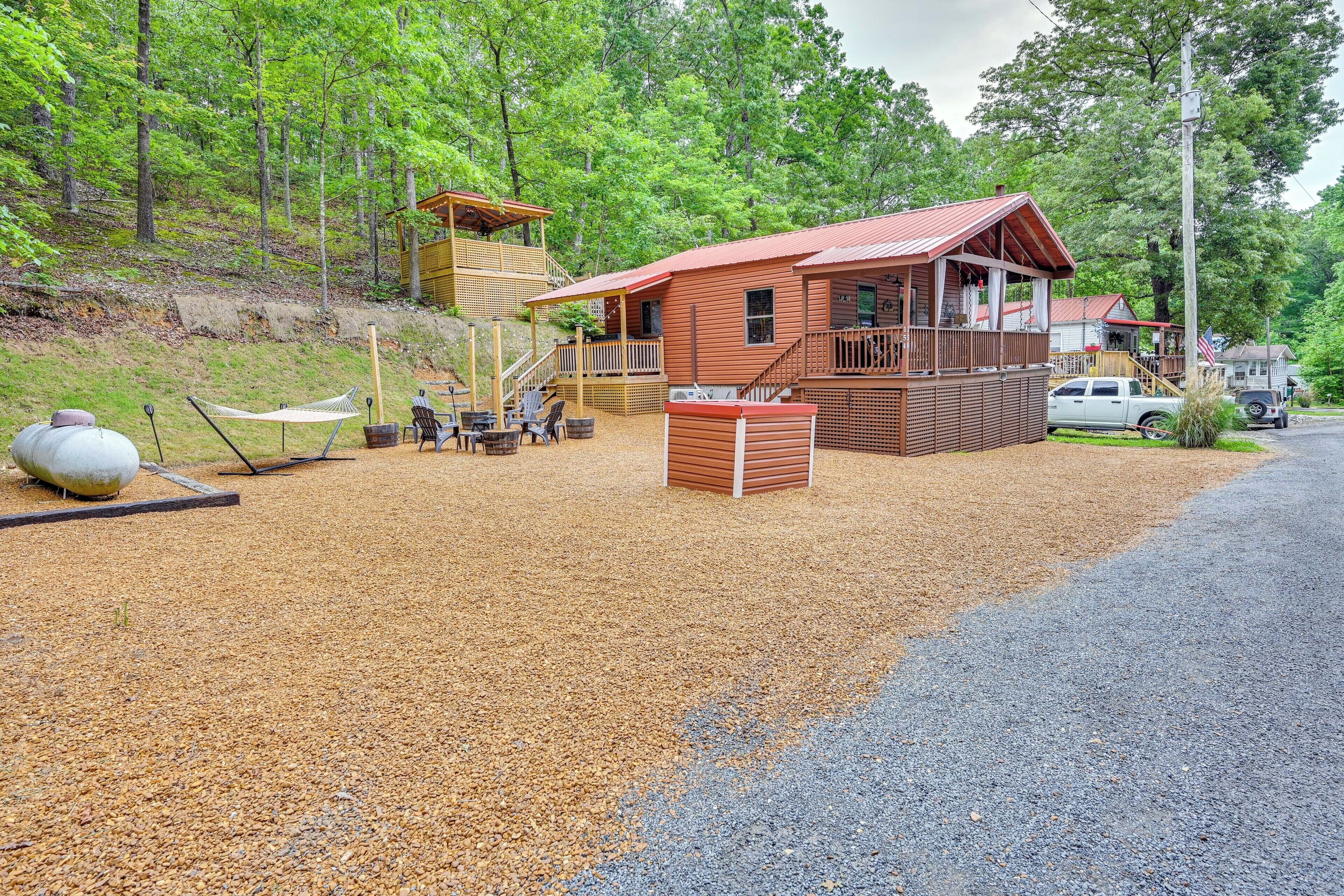 A rustic cabin with a deck, surrounded by a gravel area and a forest.
