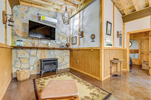 A cozy room with a stone wall, wooden beams, a fireplace, and a large window.