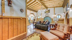A rustic interior with wooden beams, a leather sofa, a wooden coffee table, and a chandelier. - Magical 2BR Hobbit Themed House Near Gatlinburg (Cosby)