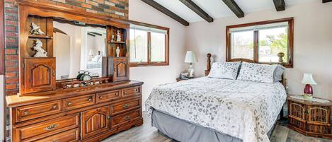 A bedroom with a large wooden dresser, a bed with a patterned bedspread, and two bedside tables with lamps.