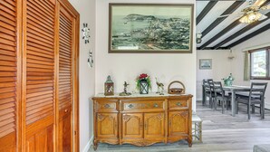 A dining area with a wooden buffet, a painting of a coastal town, and a ceiling fan. - Massachusetts Abode w/ Deck & Grill: Near Beaches! (Gloucester)
