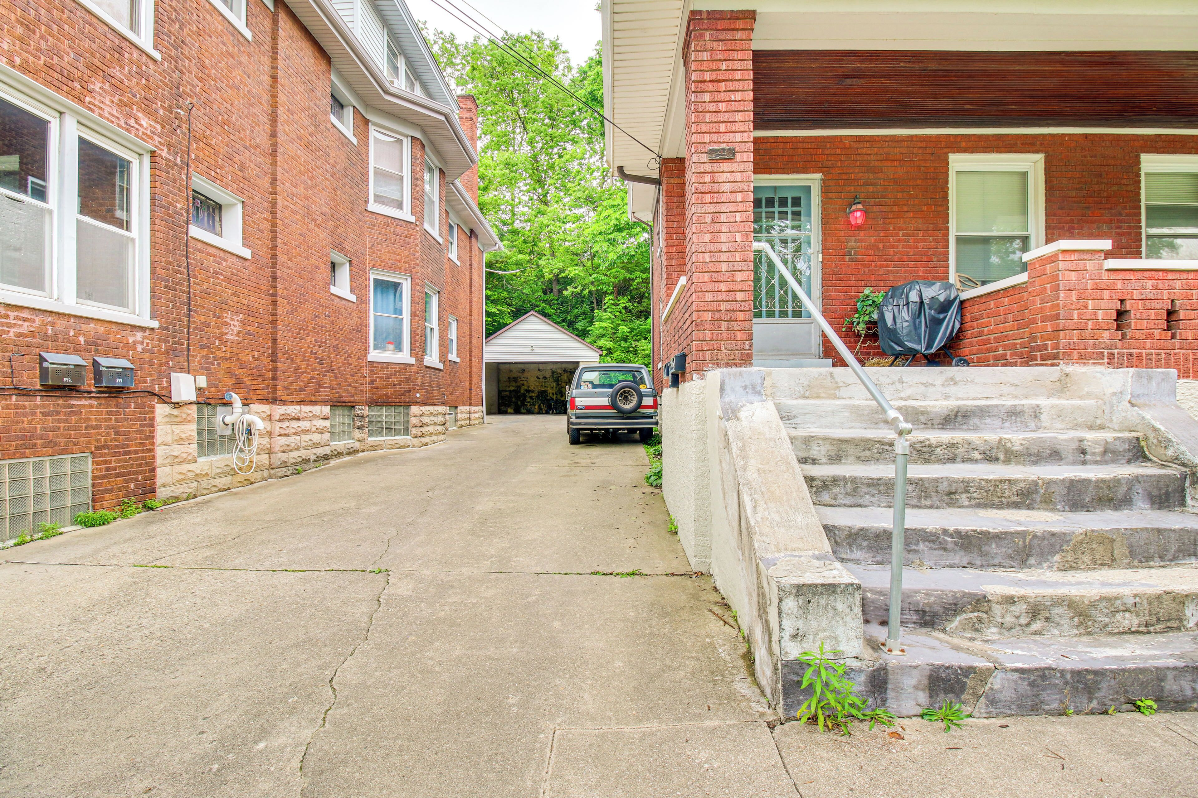 A residential street with brick buildings, a parked car, and a staircase leading to a porch.