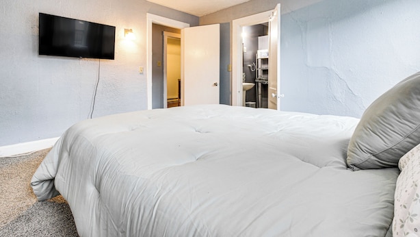 A bedroom with a large bed, a flat-screen TV mounted on the wall, and a bathroom visible through an open door. - Pet-friendly Cincinnati Apt: 5 Mi to Downtown! (Cincinnati)