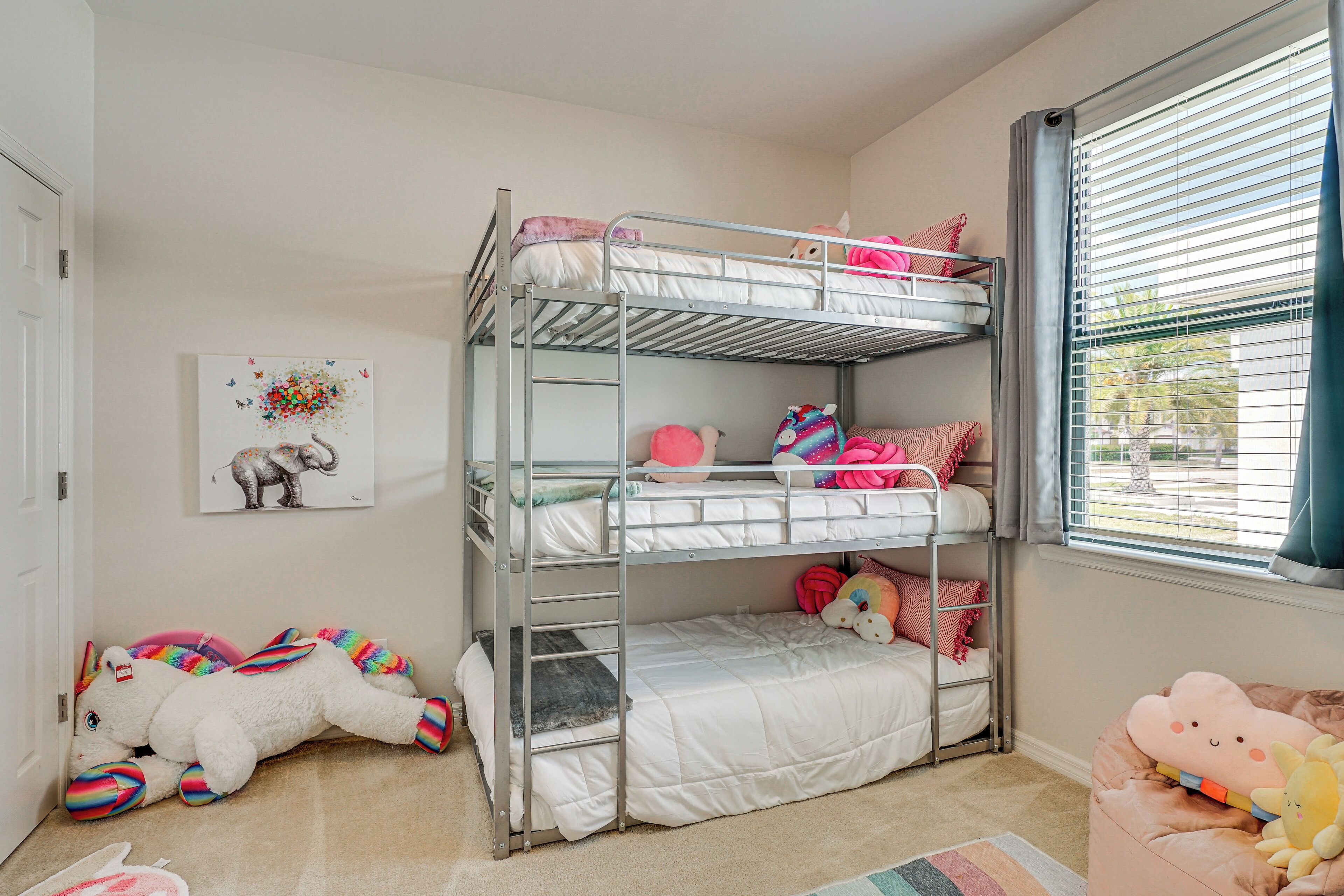 A bunk bed room with a window, a rug, and various stuffed toys.