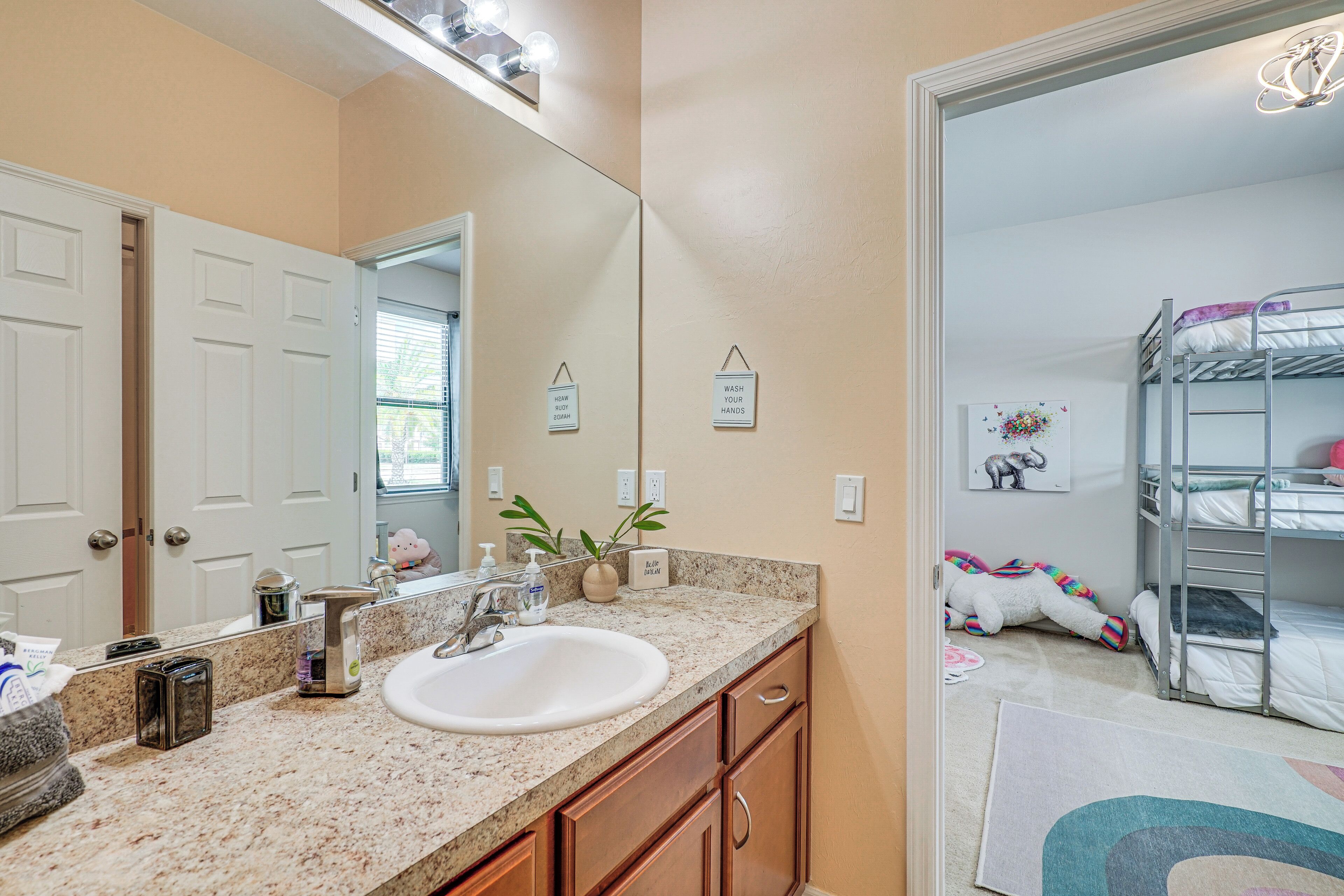 A bathroom with a sink, mirror, and a bunk bed in the adjacent room.