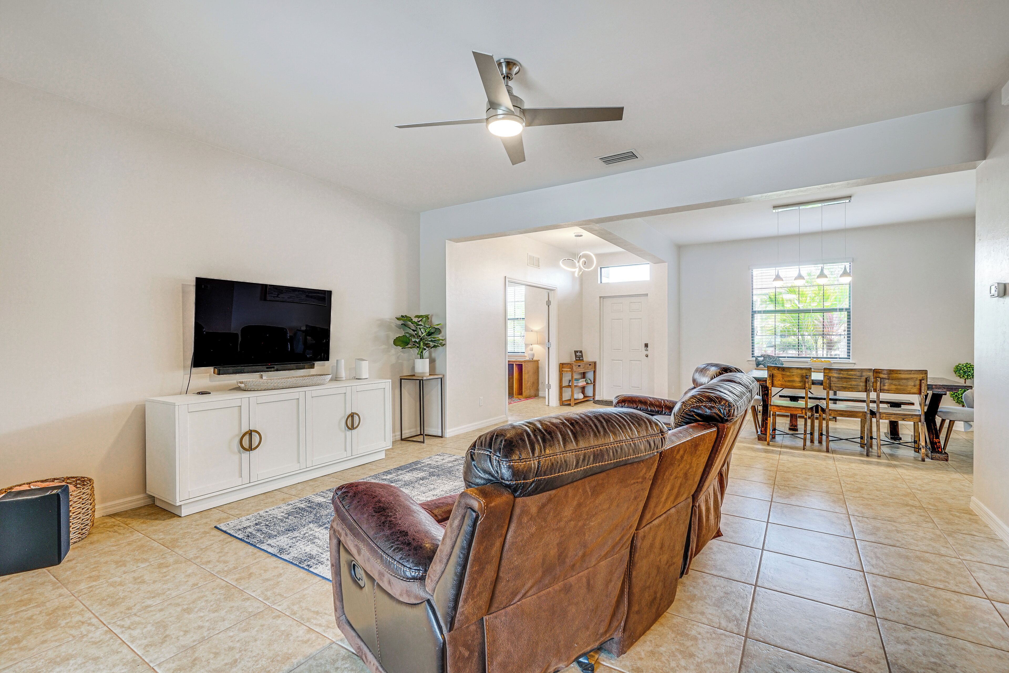 A spacious living room with a large flat-screen TV, leather recliner, dining table, and ceiling fan.
