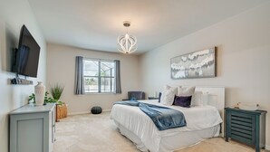 Ein Schlafzimmer mit einem großen Bett, einem an der Wand montierten Fernseher, einem Fenster mit Vorhängen, einer Deckenleuchte und einem Gemälde an der Wand.