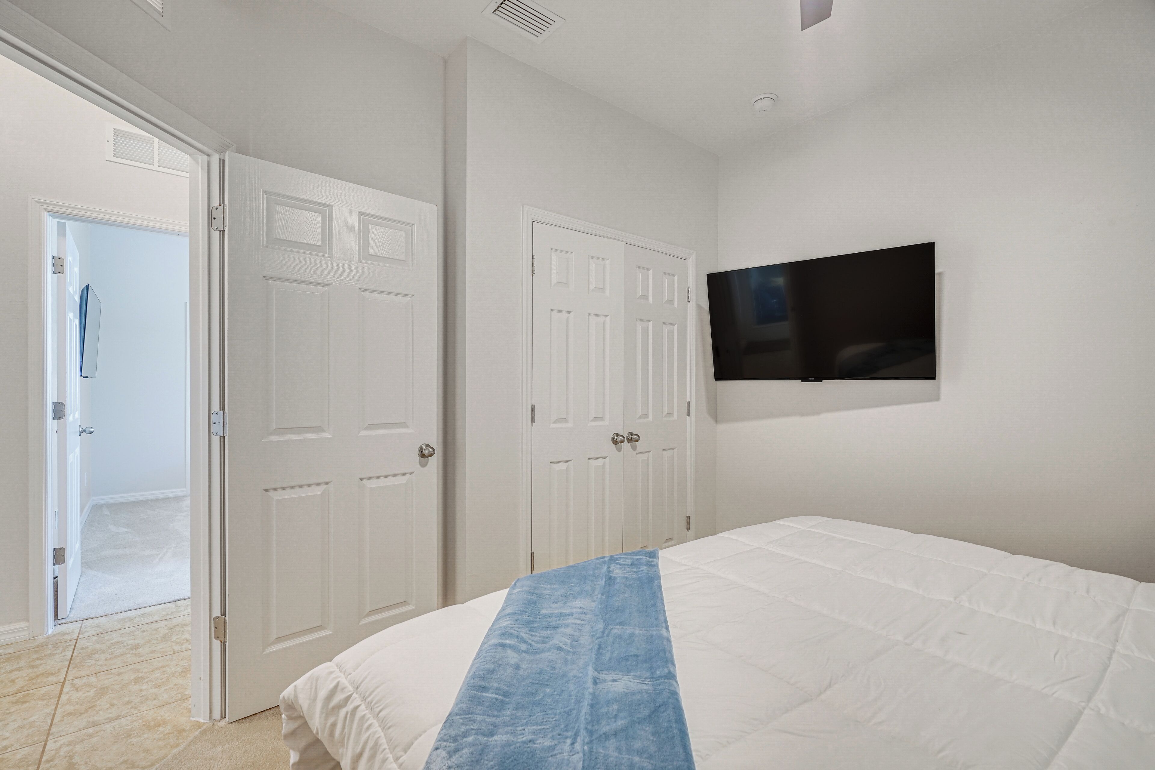Un dormitorio con cama, televisor montado en la pared y dos puertas blancas.
